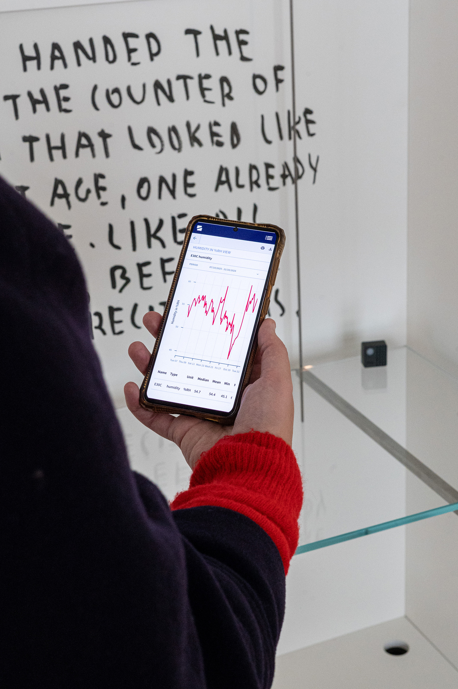 A visitor holding a phone showing Charp graphs in front of a lit display case at Abby.