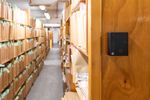 A black Charp Maxi logger on a wooden cabinet in an archive storage aisle at the Letterenhuis, Antwerp.