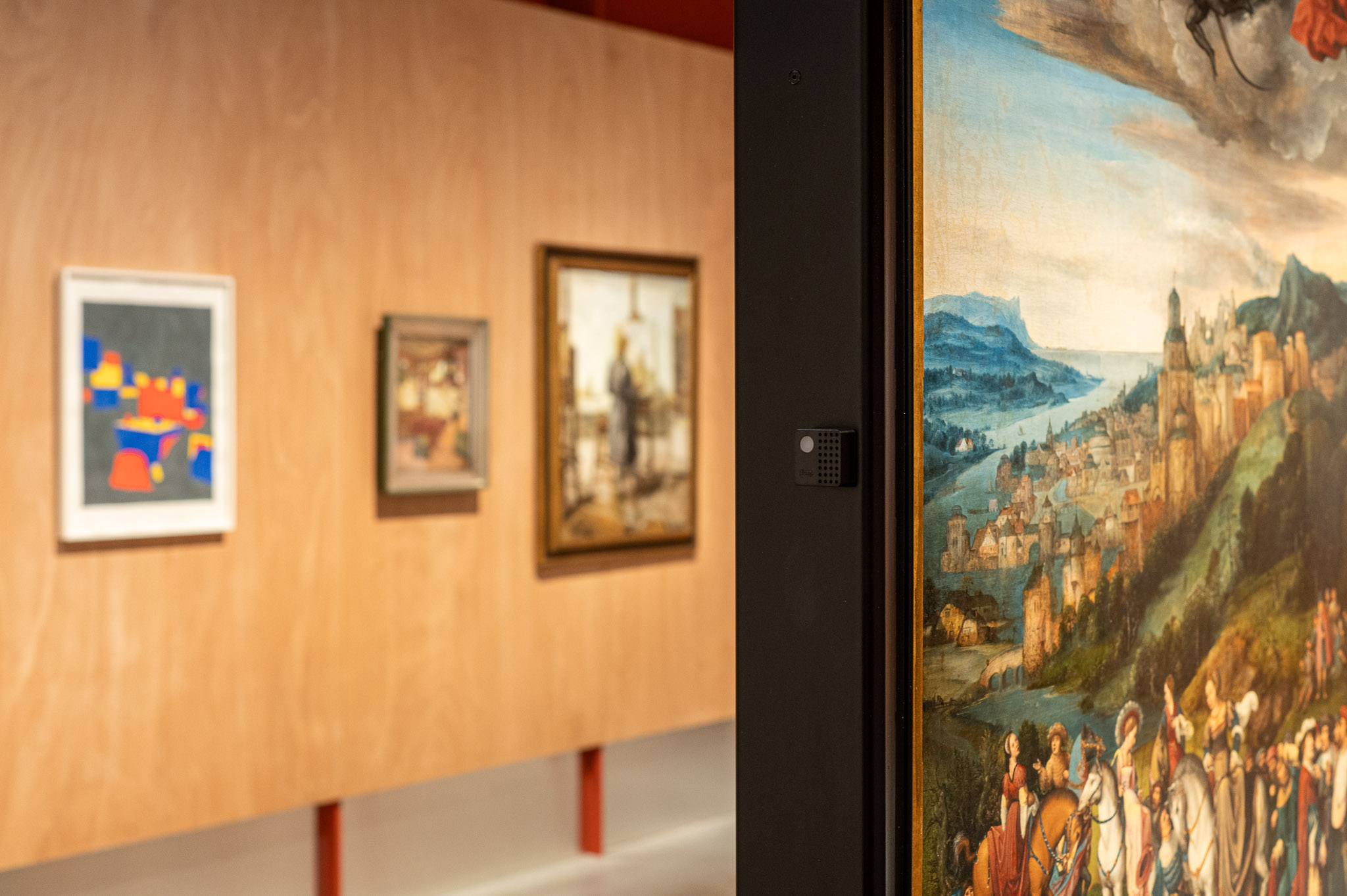 Gallery view at M Leuven with paintings hung on a wooden wall and a Charp Mini logger installed among them.