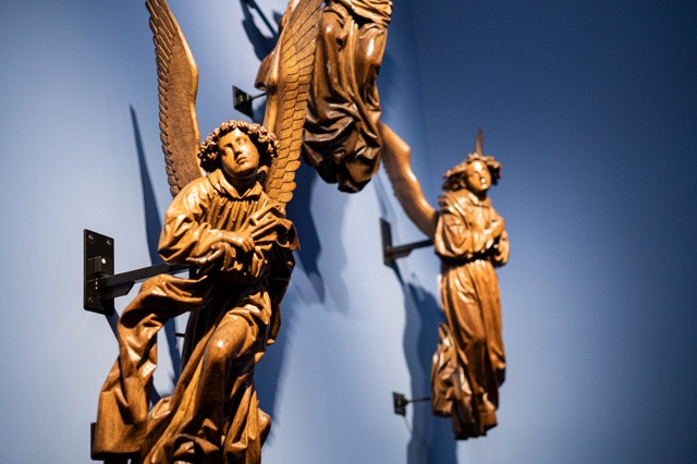 Carved wooden angel sculptures on a deep blue wall at the Maagdenhuis, Antwerp, with a Charp logger fixed discreetly to the mount.