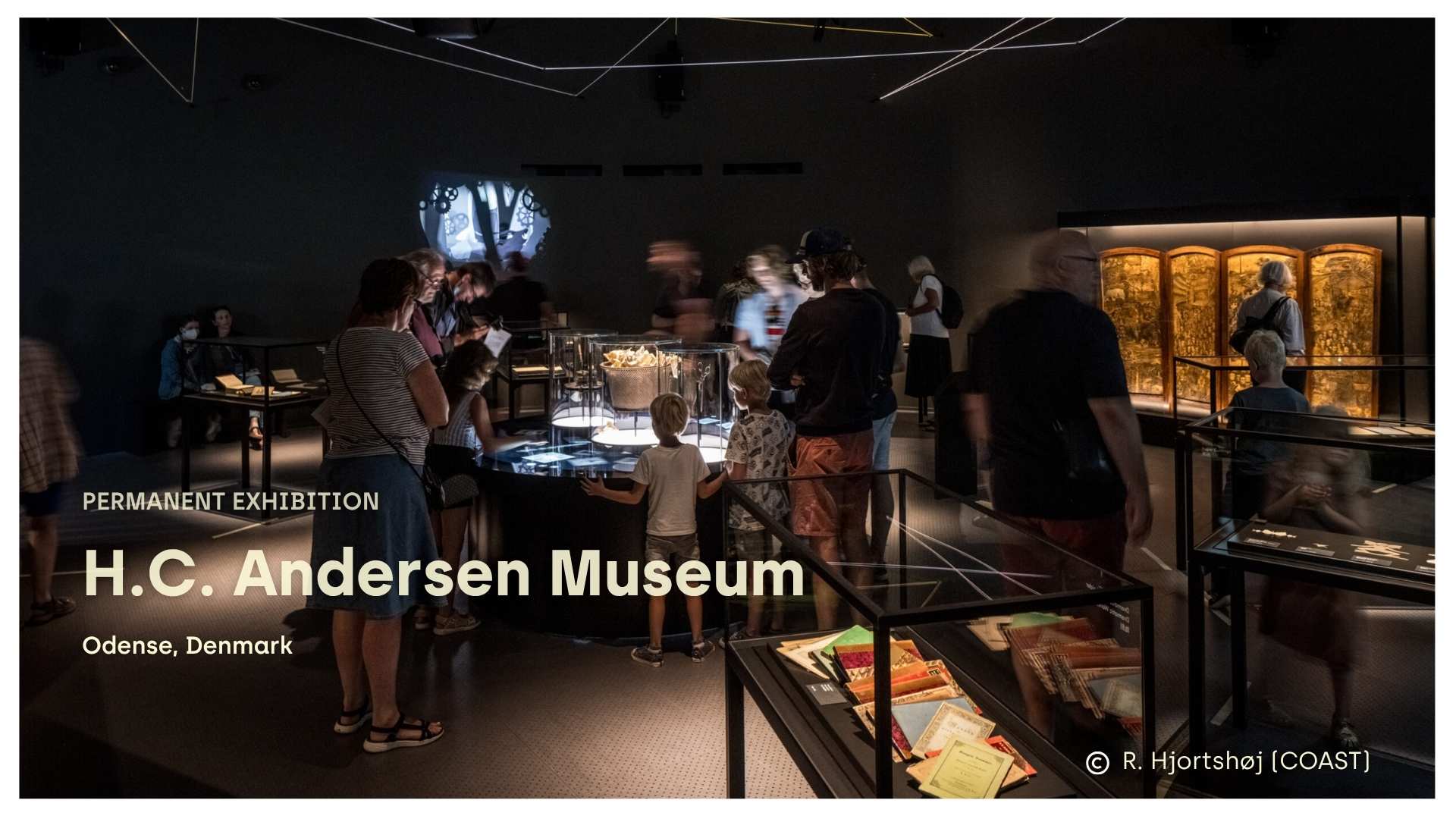 Visitors gathered around illuminated display cases in the permanent exhibition at the H.C. Andersen Museum in Odense, Denmark.